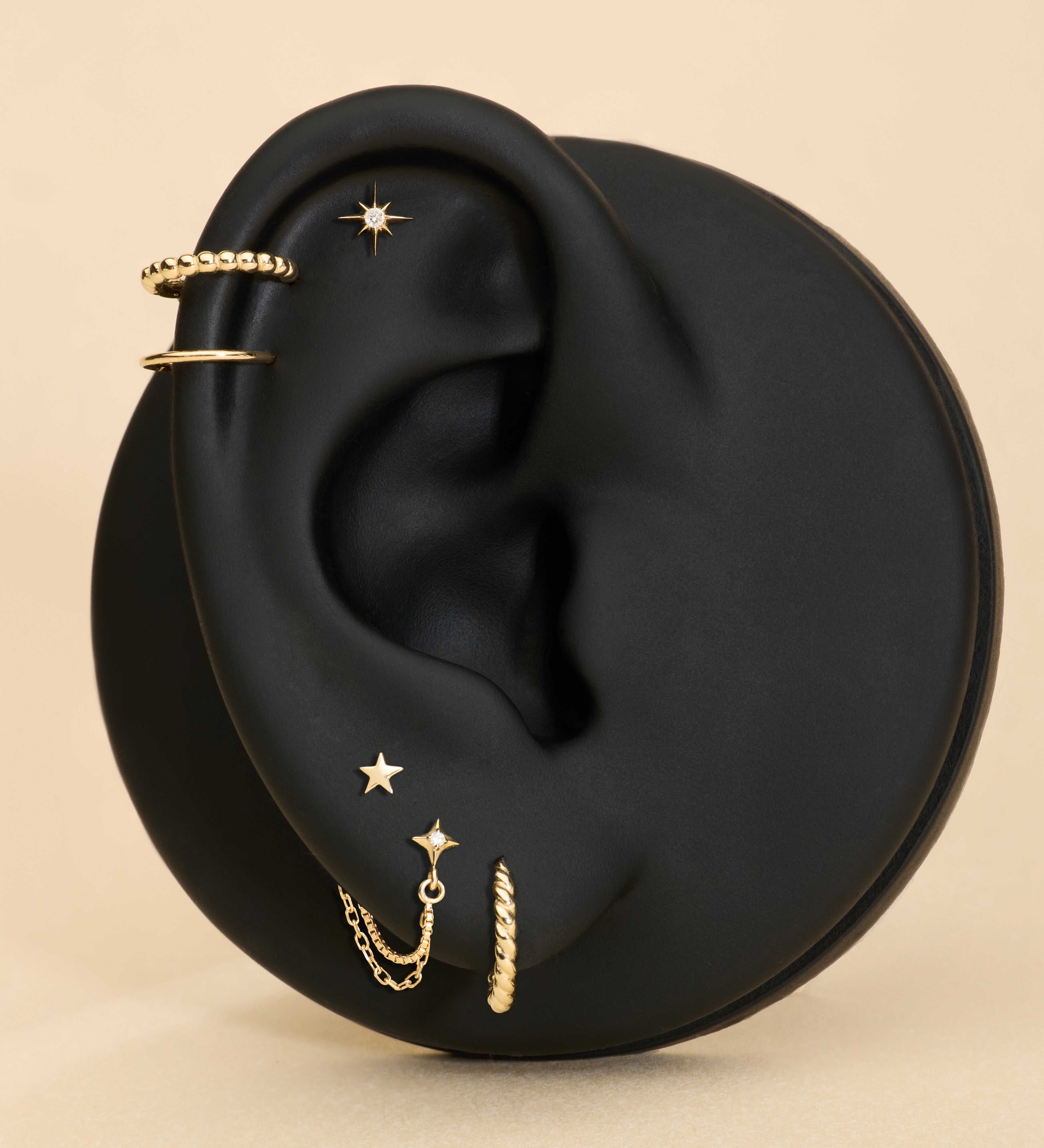 Gold earrings displayed on a black ear with a beige background