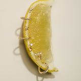 A lemon wedge displays the Lilian Crystal Heart Studs Earrings in Silver, set artfully on its surface and photographed against a neutral beige background.