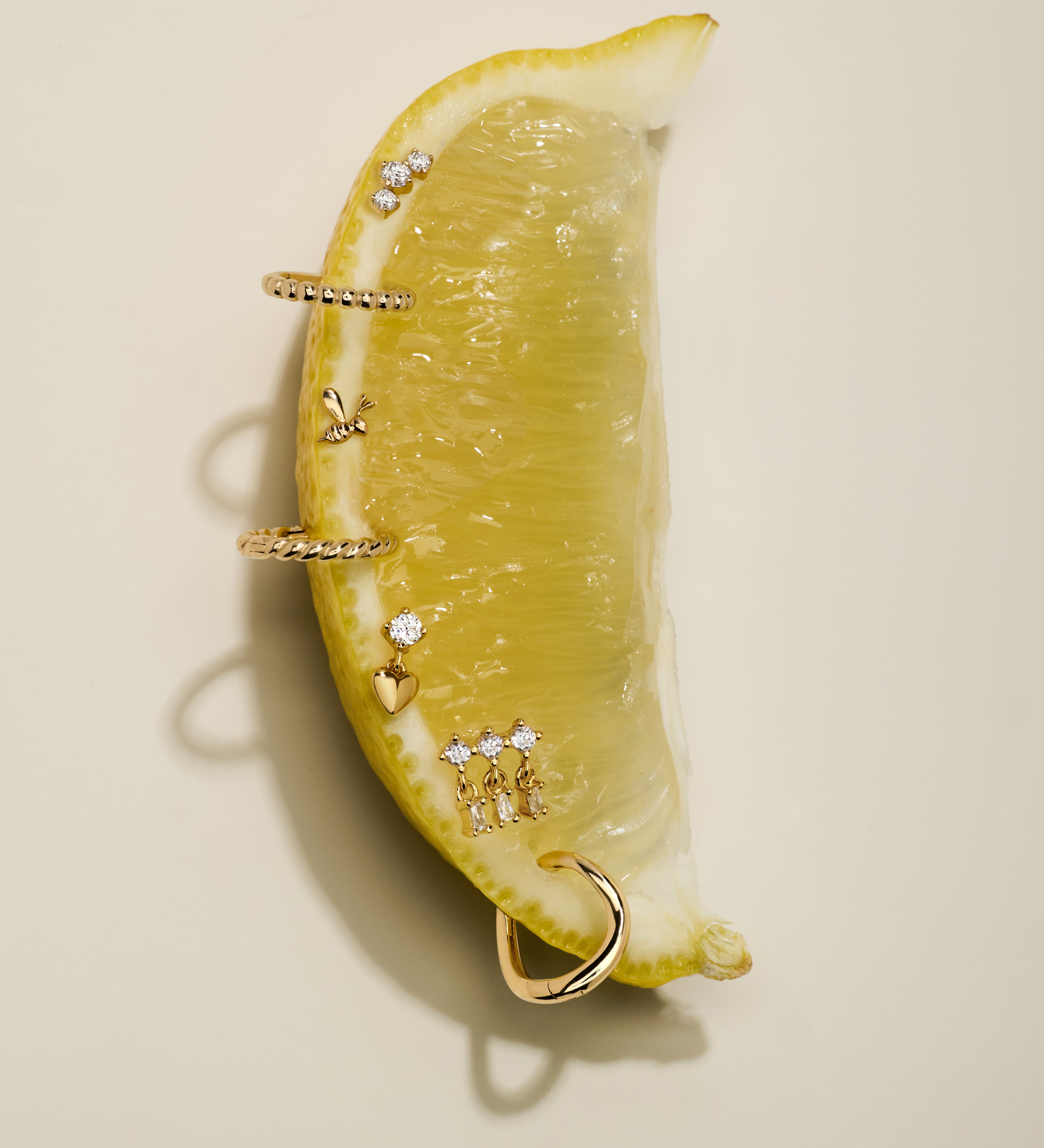 A lemon wedge displays the Lilian Crystal Heart Studs Earrings in Silver, set artfully on its surface and photographed against a neutral beige background.