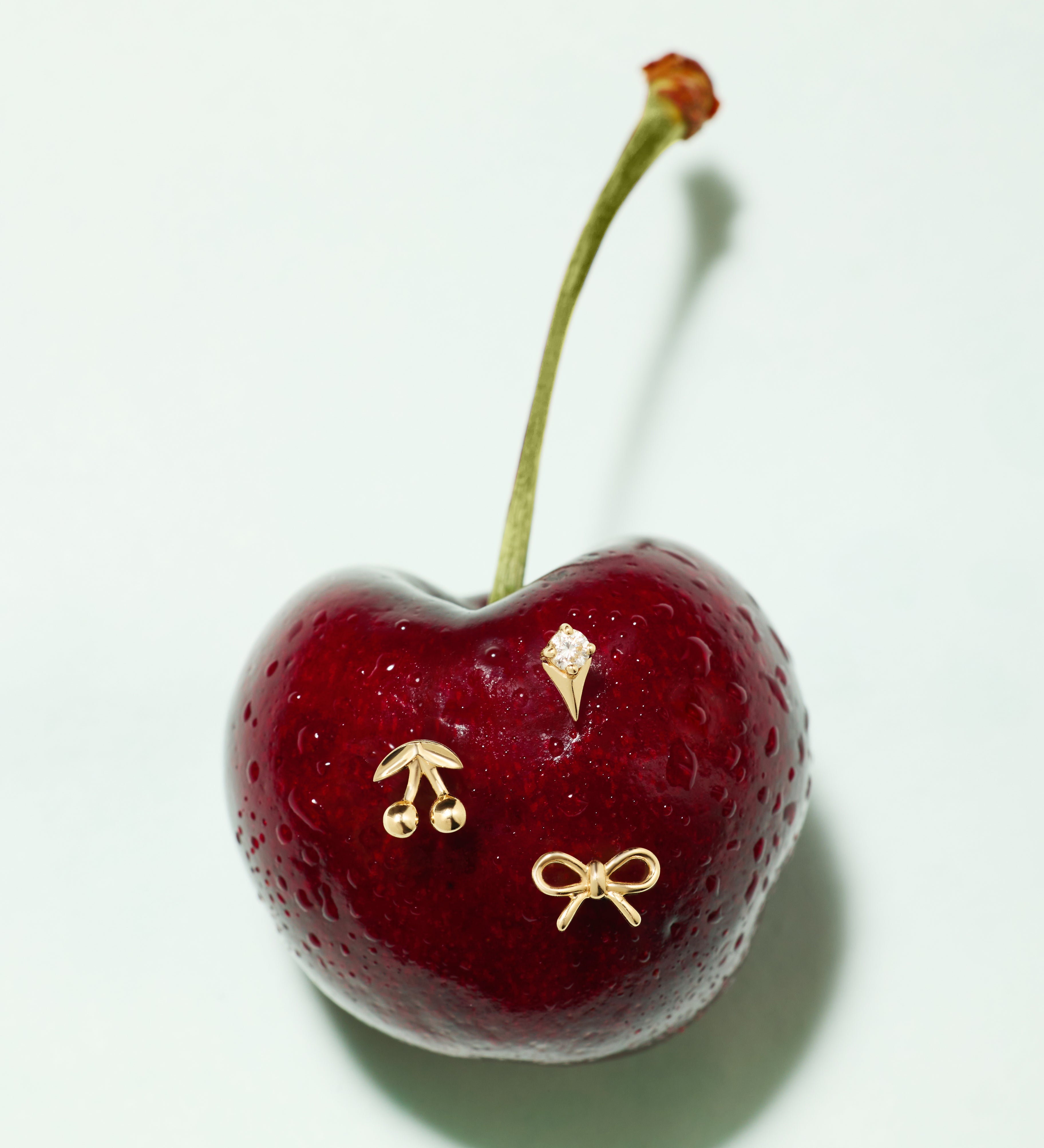 The 14K Solid Yellow Gold Cherry Flat Back Stud features a single cherry with three small 14k gold stud pins—a cherry, an ice cream cone, and a bow—set on a plain white background.
