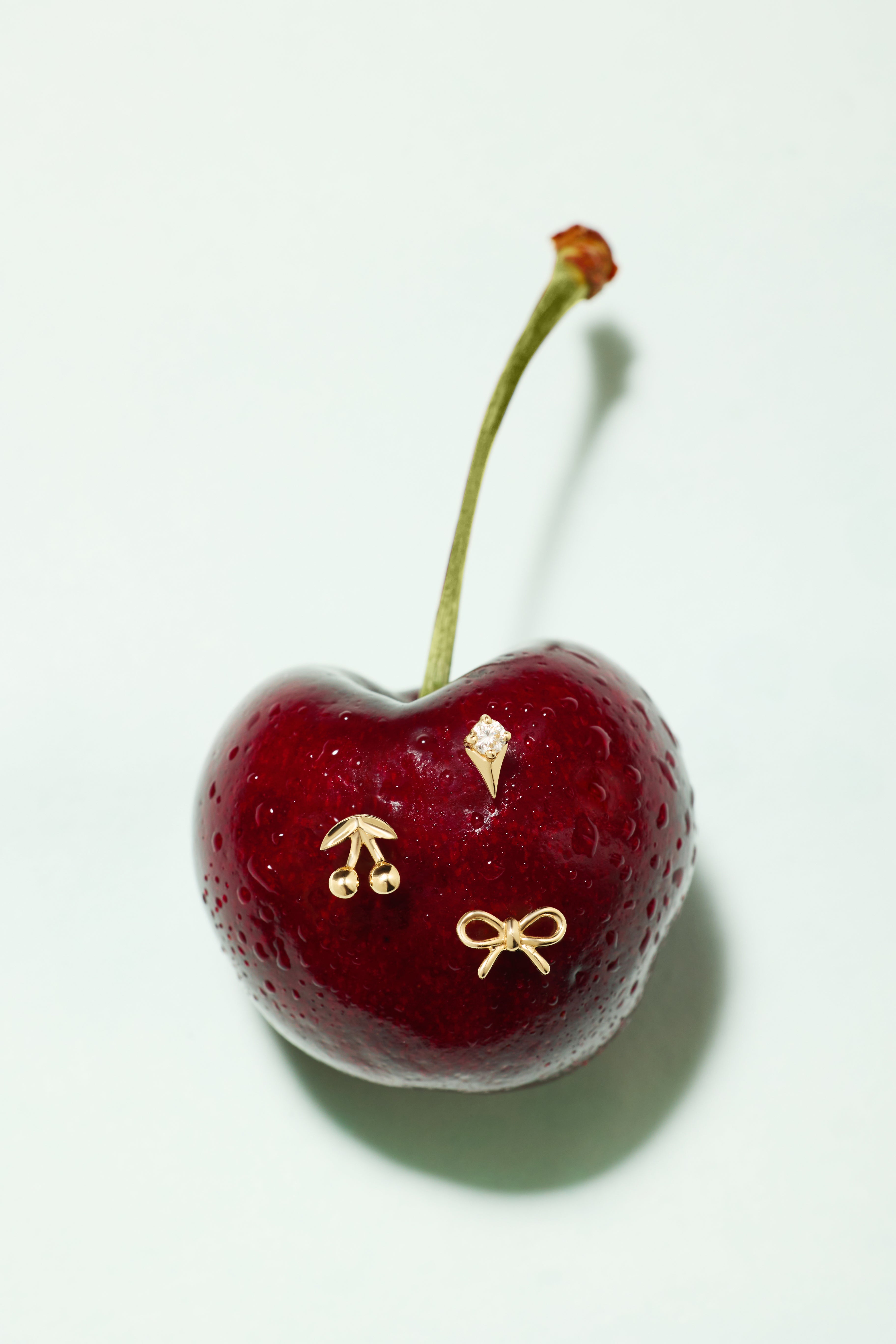 The 14K Solid Yellow Gold Cherry Flat Back Stud features a single cherry with three small 14k gold stud pins—a cherry, an ice cream cone, and a bow—set on a plain white background.