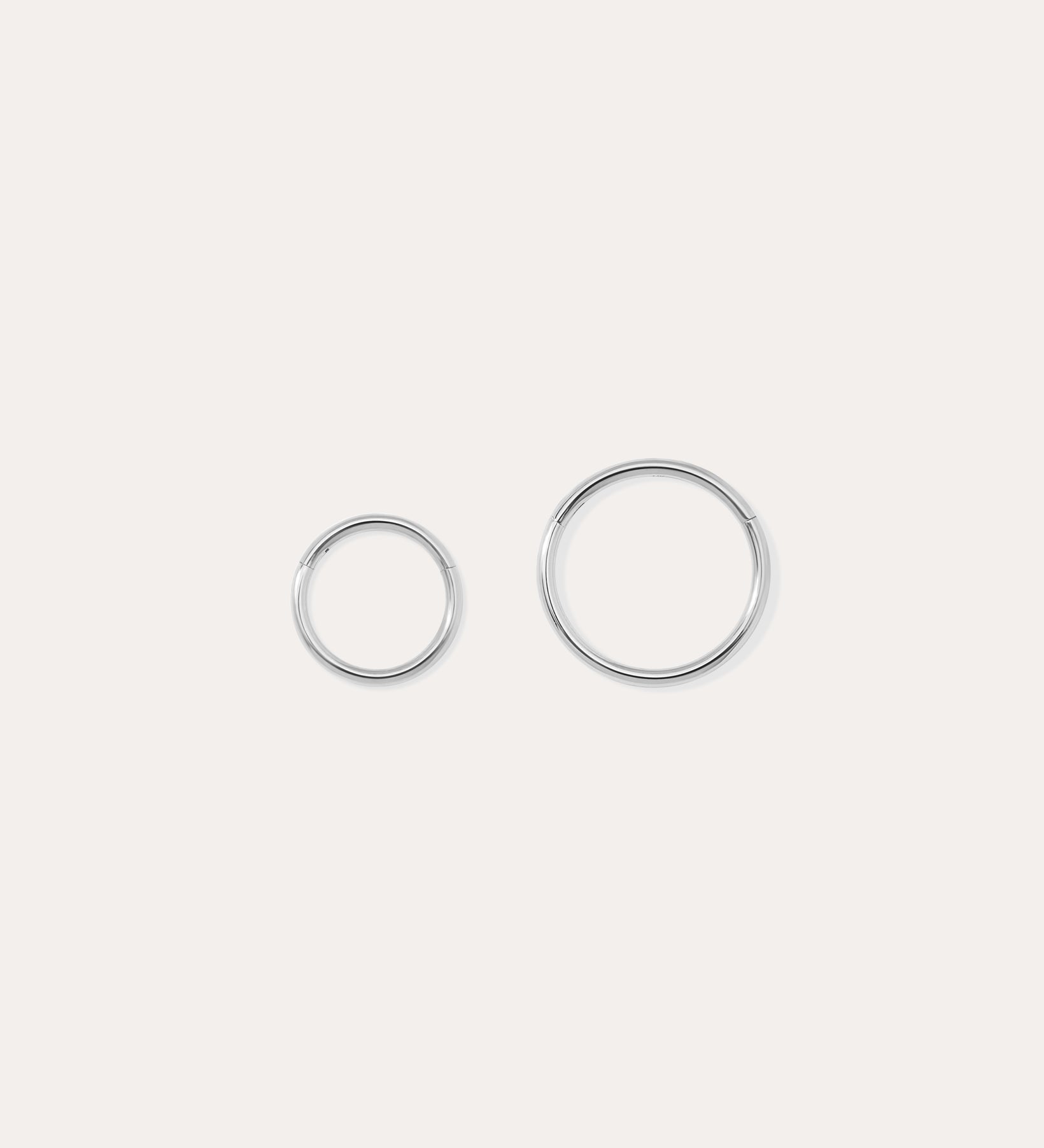 The 14K Solid White Gold 20G Mini Clicker, shown in two shiny sizes on a plain white background, is perfect for use as a clicker or nose ring.