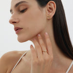 A woman with straight dark hair poses in profile wearing minimal makeup, a gold geometric hoop earring, and the Reneé Minimalist Triangle Ring in Gold, which adorns her hand as she gently touches her neck.