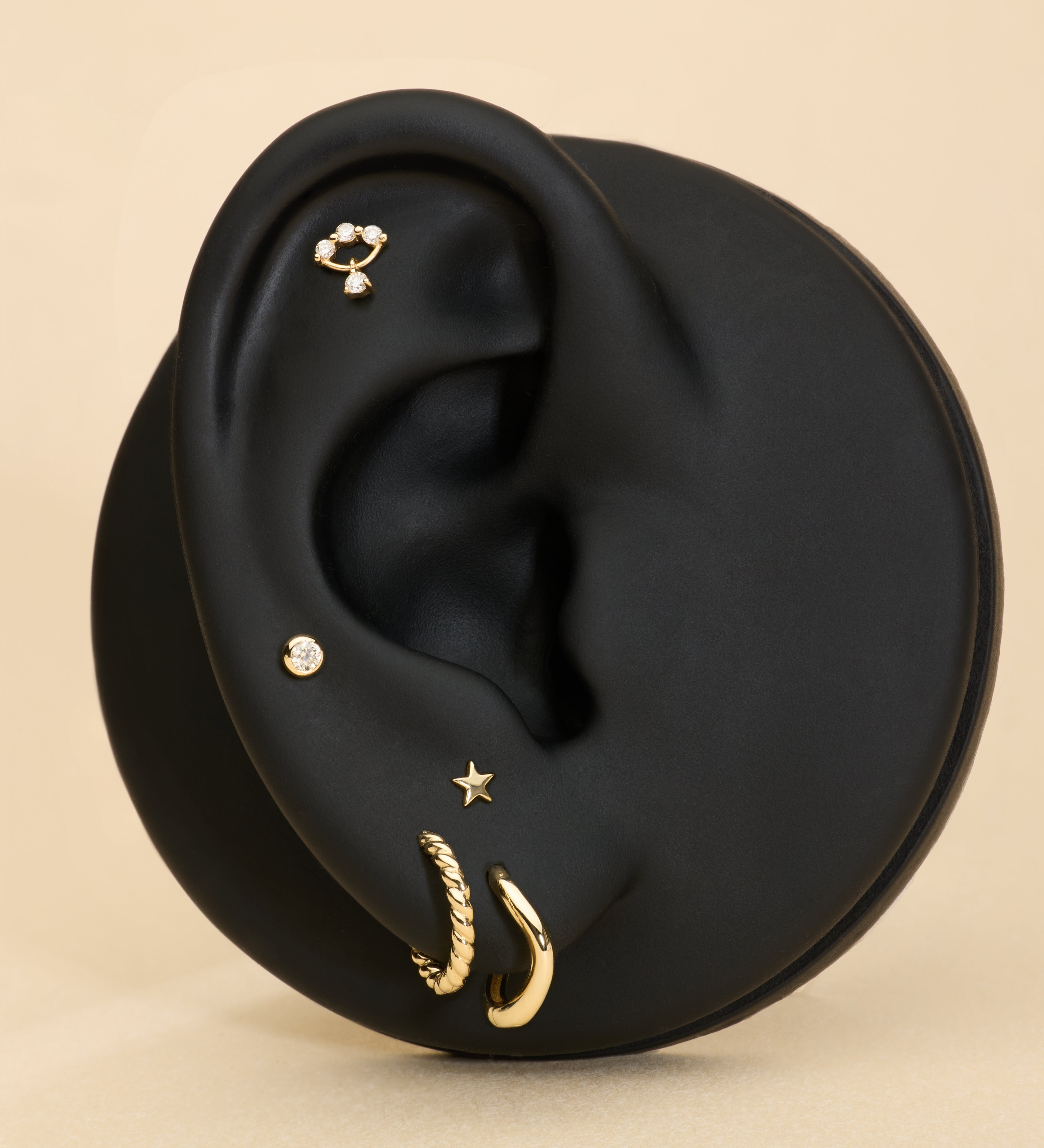 Black ear with gold earrings on a beige background with solid gold flatback studs