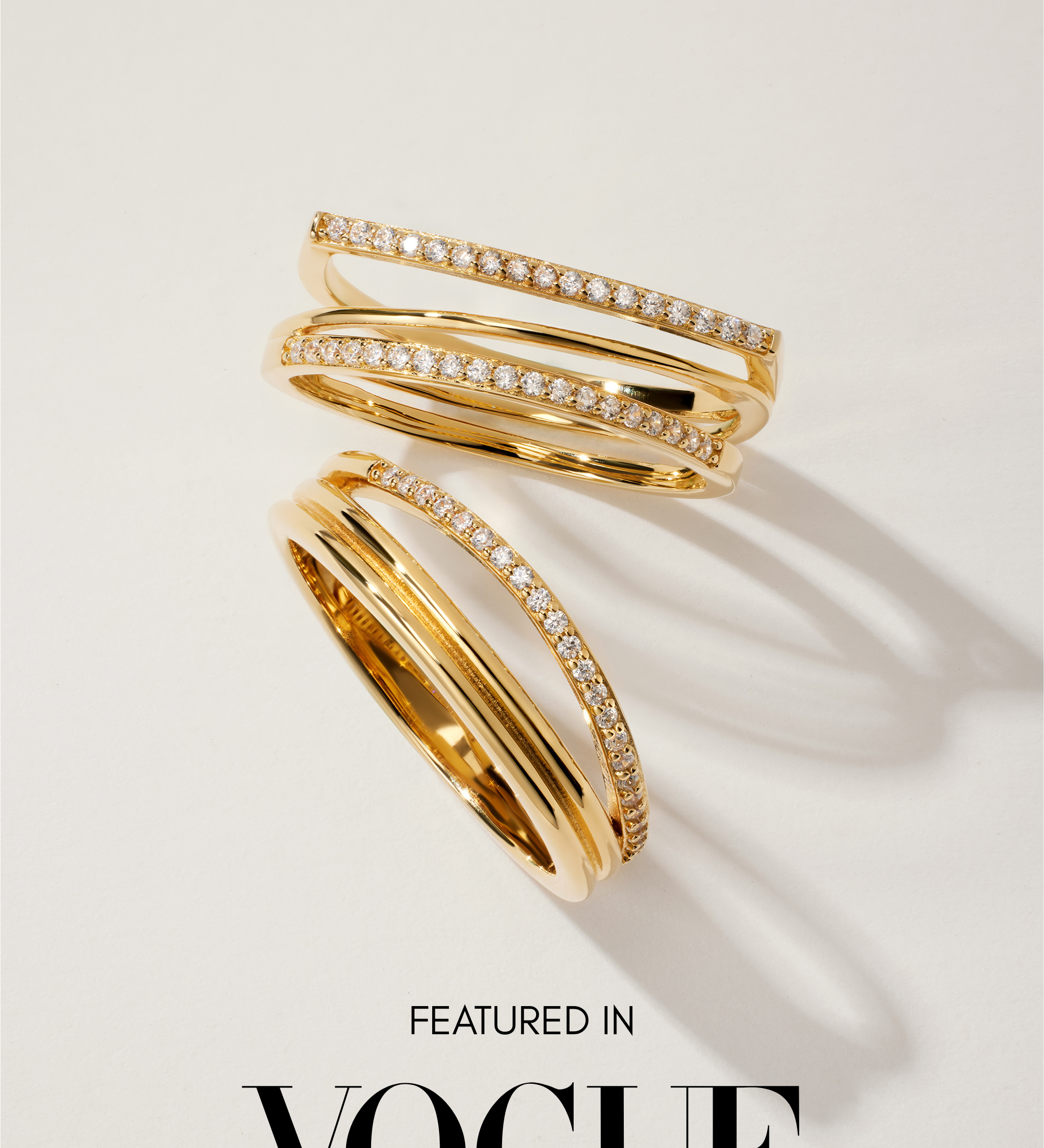The Noor Pavé Triple Band Rings in Gold, featuring rows of sparkling pavé diamonds, are displayed on a white surface with soft shadows. Below the rings, the text reads Featured in VOGUE.