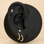 Black ear with gold stud cherry earrings and gold heart flat back stud on a beige background