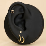 Black ear with gold stud cherry earrings and gold heart flat back stud on a beige background