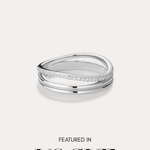 The Noor Pavé Triple Band Ring in Silver, featuring a modern curved design and a row of pavé diamonds, sits centered on a light background. Below the ring, black text reads FEATURED IN VOGUE.