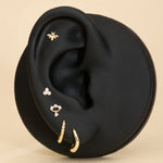 Black ear with gold huggie earrings, bee flatback stud, and diamond flatback stud on a beige background