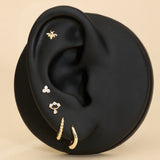 Black ear with gold huggie earrings, bee flatback stud, and diamond flatback stud on a beige background