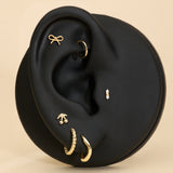 Ear with gold earrings, bow stud, cheery stud and diamond stud on a beige background