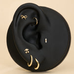Ear with gold earrings, bow stud, cheery stud and diamond stud on a beige background