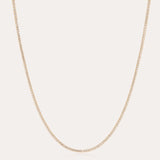 The Alba Tennis Necklace in Gold features a thin, simple design with fine links and a subtle shine, shown in a gentle curve against a light background.