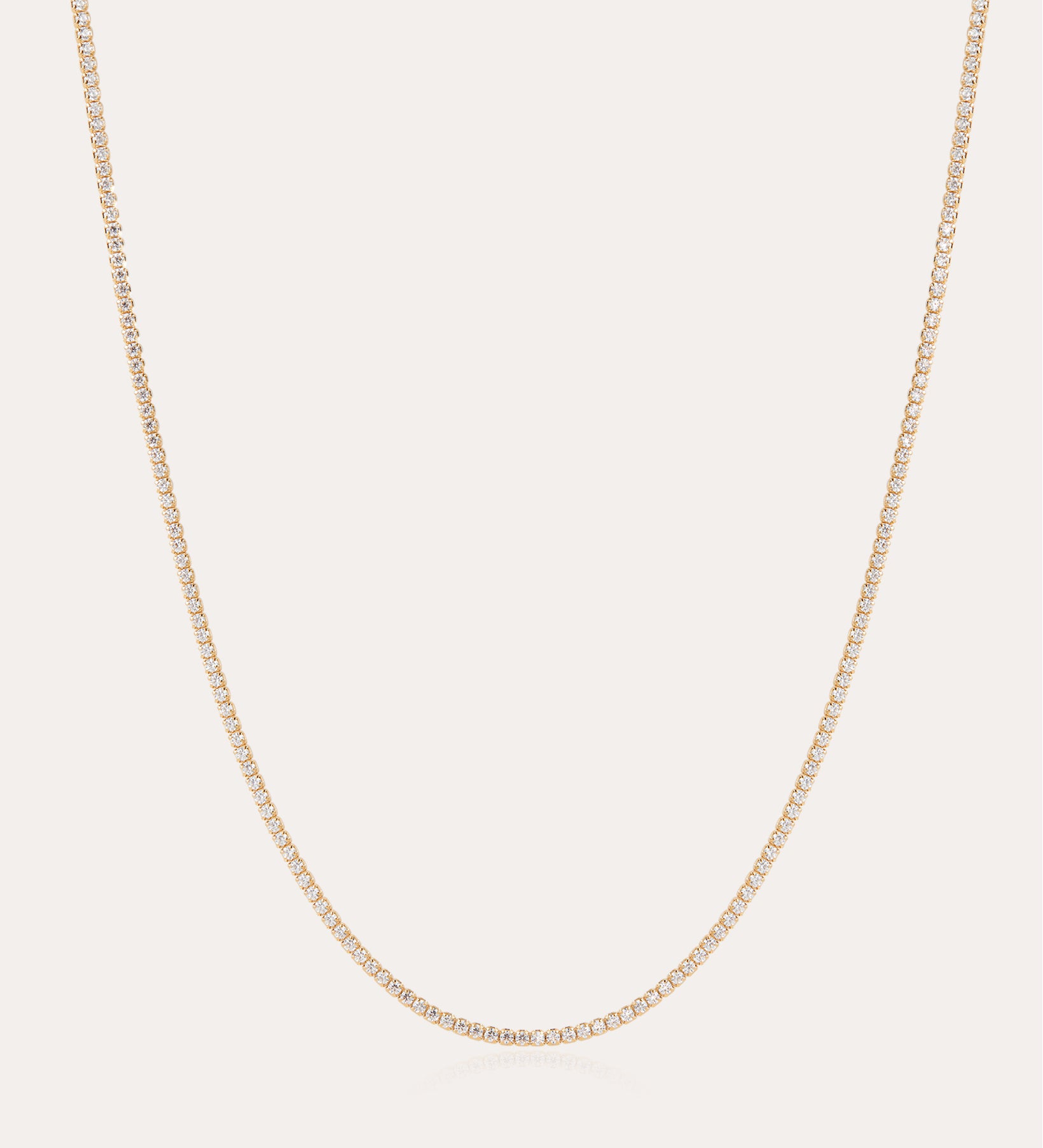 The Alba Tennis Necklace in Gold features a thin, simple design with fine links and a subtle shine, shown in a gentle curve against a light background.