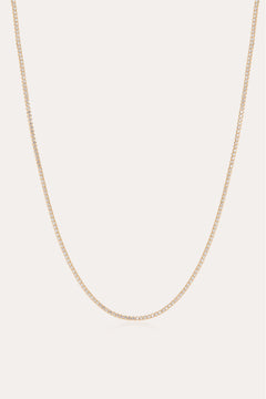 The Alba Tennis Necklace in Gold features a thin, simple design with fine links and a subtle shine, shown in a gentle curve against a light background.