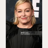 A woman with shoulder-length blonde hair smiles at an event, wearing a black dress and the Judith Hexagon Angular Huggies in Silver. She stands before a gray background with bold white letters. Text reads: Spotted on: Christine Tremarco.