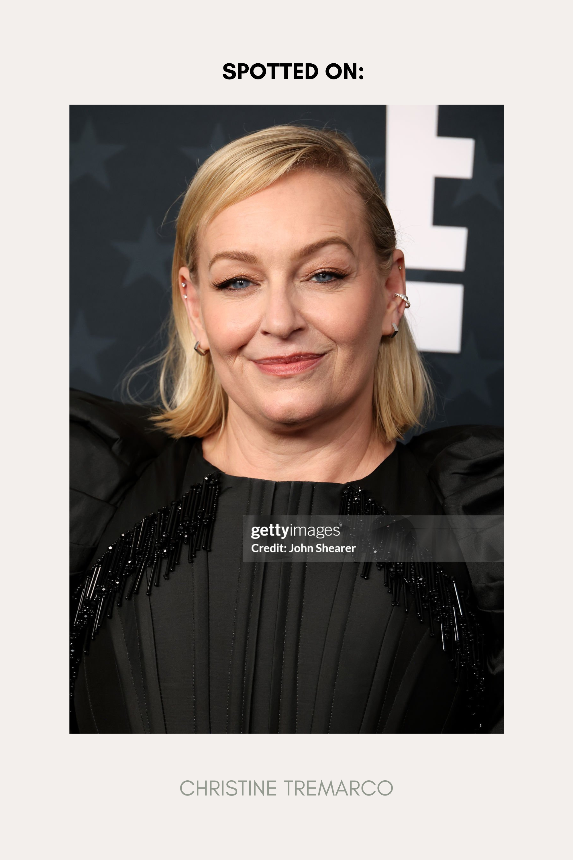 A woman with shoulder-length blonde hair smiles at an event, wearing a black dress and the Judith Hexagon Angular Huggies in Silver. She stands before a gray background with bold white letters. Text reads: Spotted on: Christine Tremarco.