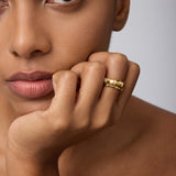 A close-up of a woman with smooth, brown skin resting her chin on her hand, wearing the Bamboo Ring in Gold on her index finger as she gazes calmly past the camera.