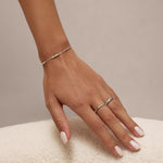 A hand with pale pink manicured nails rests on a soft, white textured surface, adorned with the Bamboo Chain Bracelet in Silver and two S925 sterling silver rings on the middle and ring fingers.