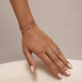 A hand with pale pink manicured nails rests on a soft, white textured surface, adorned with the Bamboo Chain Bracelet in Silver and two S925 sterling silver rings on the middle and ring fingers.