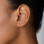 Close-up of an ear adorned with four gold earrings: a 14K Solid Yellow Gold Bow Tie Flat Back Stud at the top and three minimalist hoops along the earlobe. The person has smooth skin and dark hair pulled back.