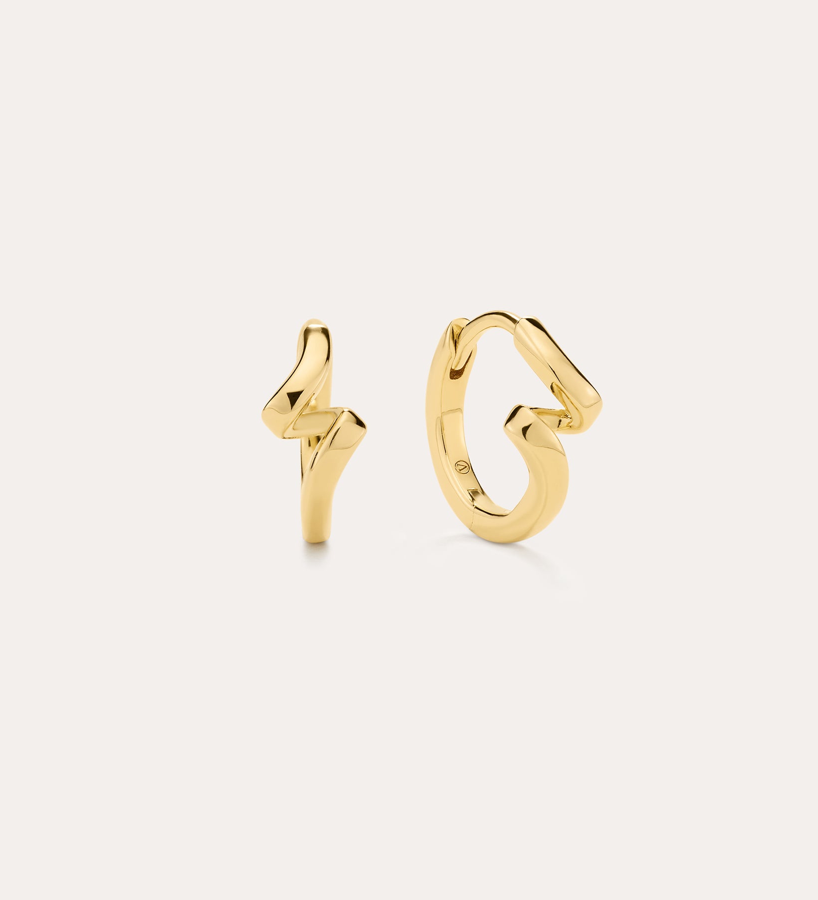 The image shows two small 18k gold plated stud earrings—one a lightning bolt, the other a looping squiggle—styled with Ribbon Twist Huggies in Gold, all set against an off-white background for a chic presentation.