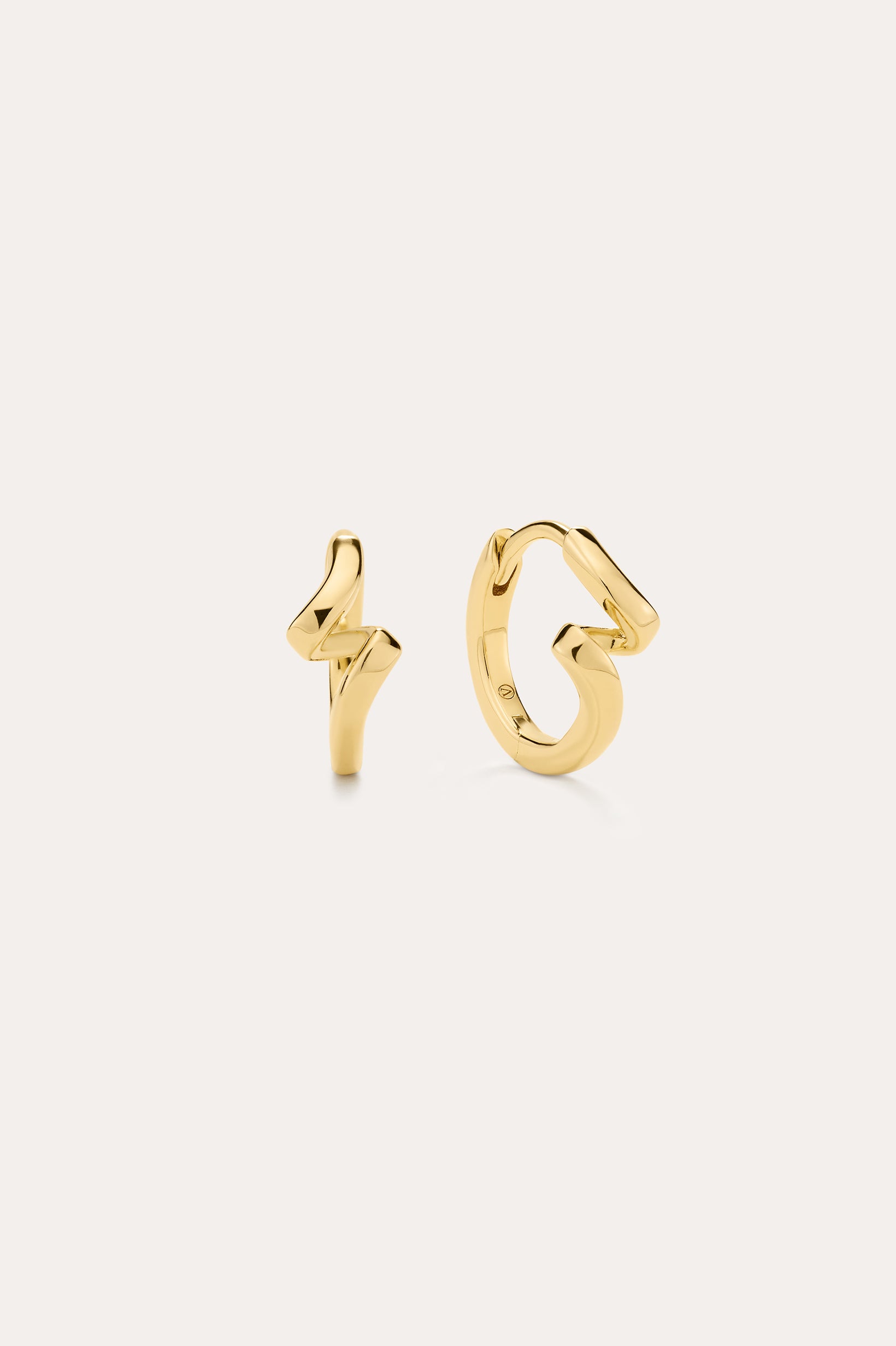 The image shows two small 18k gold plated stud earrings—one a lightning bolt, the other a looping squiggle—styled with Ribbon Twist Huggies in Gold, all set against an off-white background for a chic presentation.