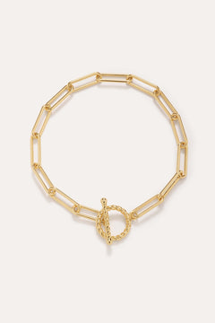 The Paperclip Toggle Bracelet in Gold, crafted in 18k gold plated finish with elongated oval links and a twisted toggle clasp, is shown against a plain light background.