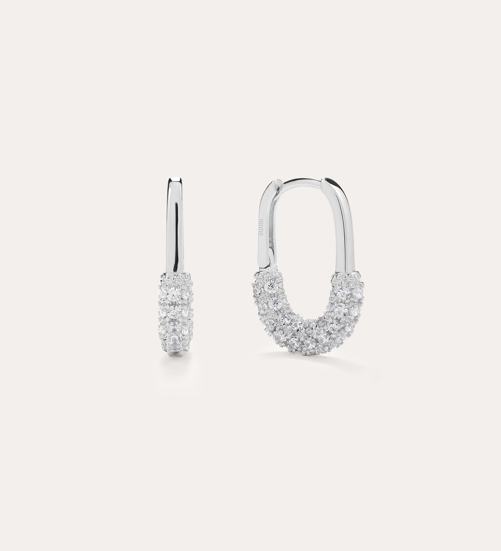 The Nouf Pavé Hoop Earrings in Sterling Silver, partially adorned with sparkling cubic zirconia, are shown on a plain light background—one earring displayed from the front, the other from the side.