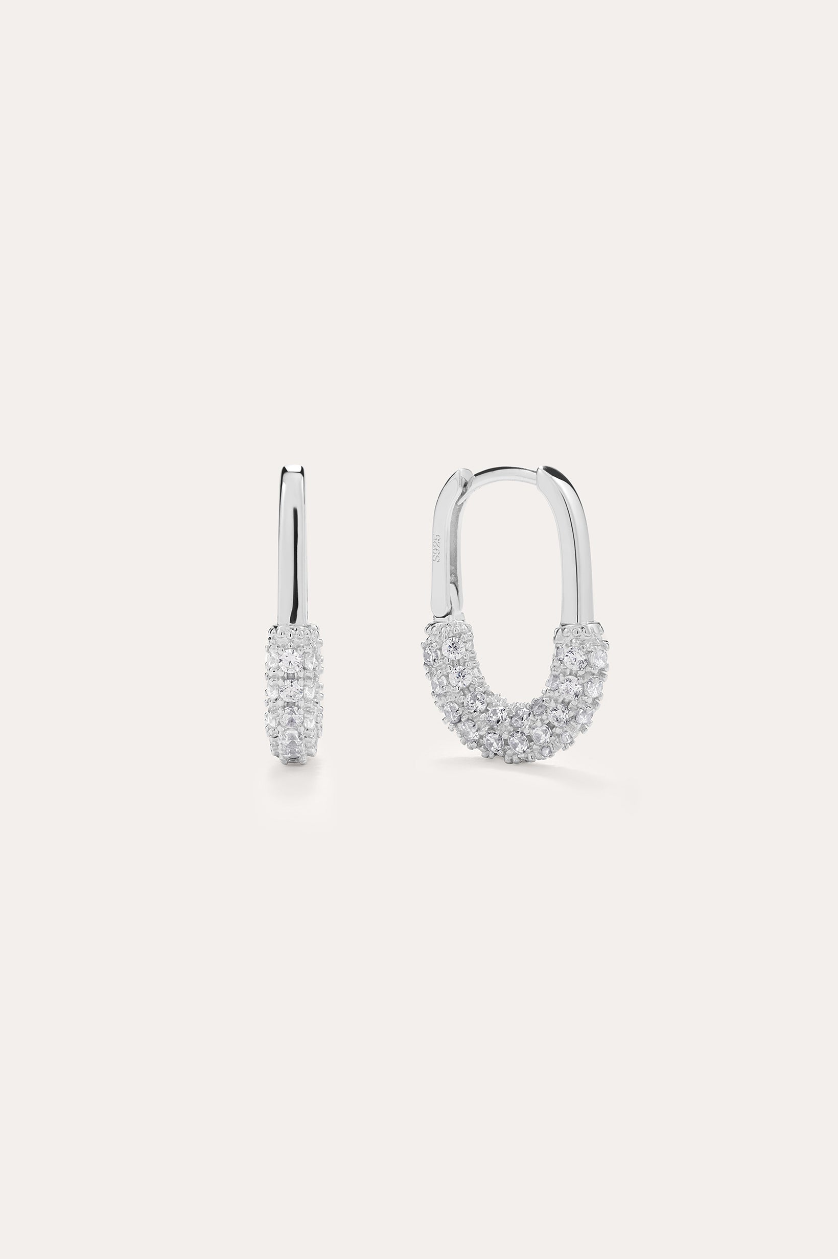 The Nouf Pavé Hoop Earrings in Sterling Silver, partially adorned with sparkling cubic zirconia, are shown on a plain light background—one earring displayed from the front, the other from the side.