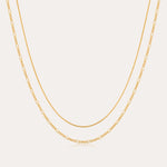 The Figaro And Box Chain Layered Necklace in 18k Gold Plated features a dual design: a sleek box chain above and elongated Figaro links below, beautifully displayed against a white background for an elegant layered look.