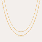 The Figaro And Box Chain Layered Necklace in 18k Gold Plated features a dual design: a sleek box chain above and elongated Figaro links below, beautifully displayed against a white background for an elegant layered look.