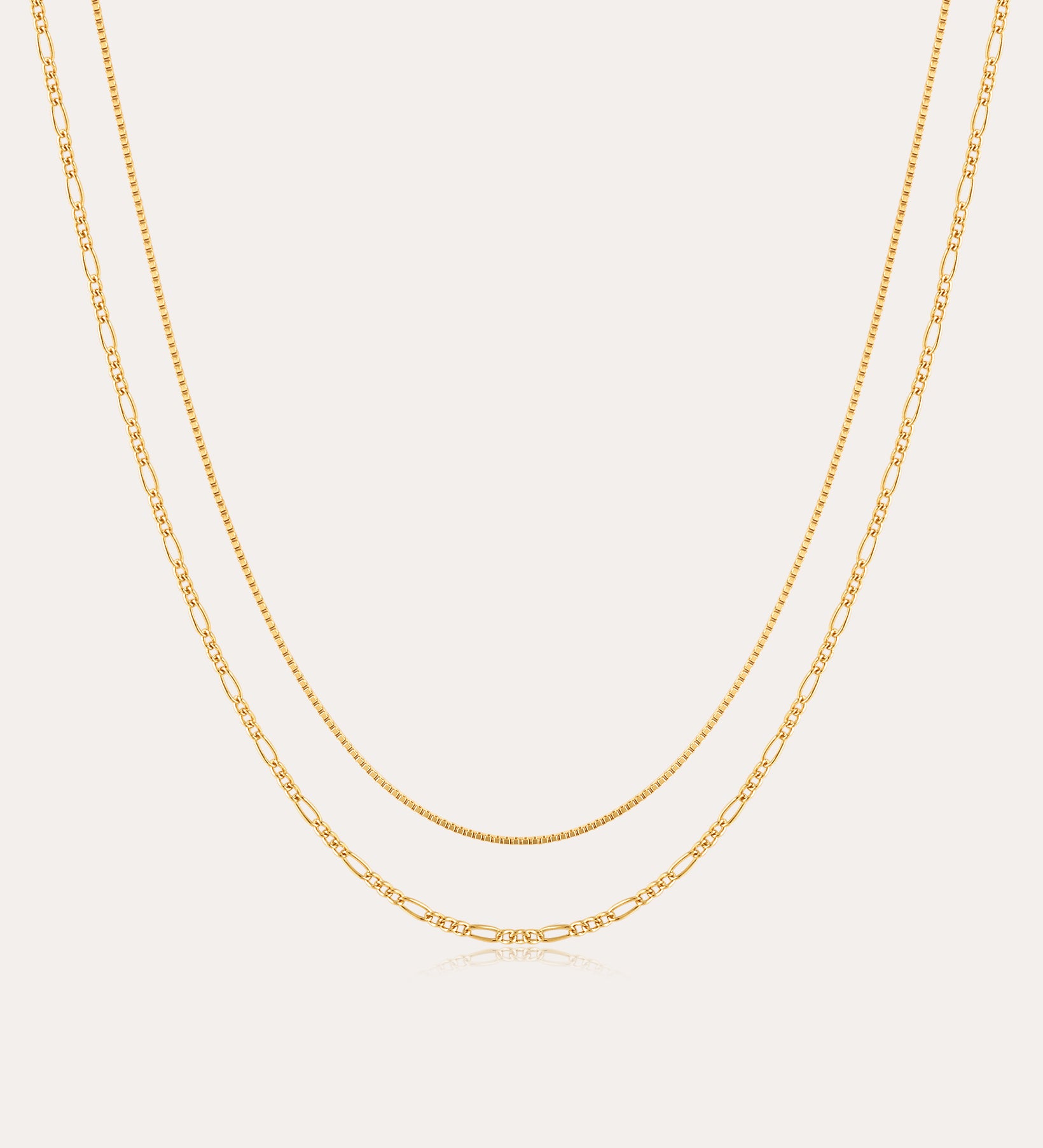 The Figaro And Box Chain Layered Necklace in 18k Gold Plated features a dual design: a sleek box chain above and elongated Figaro links below, beautifully displayed against a white background for an elegant layered look.