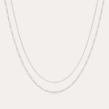 The Figaro And Box Chain Layered Necklace in Sterling Silver features a fine box chain and a longer Figaro link, both displayed against a plain white background for an elegant layered look.