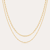The Mini Paperclip Double Chain Necklace in Gold features two 18k gold plated layered chains—one with delicate elongated links, the other with fine round links—displayed elegantly against a plain, light background.