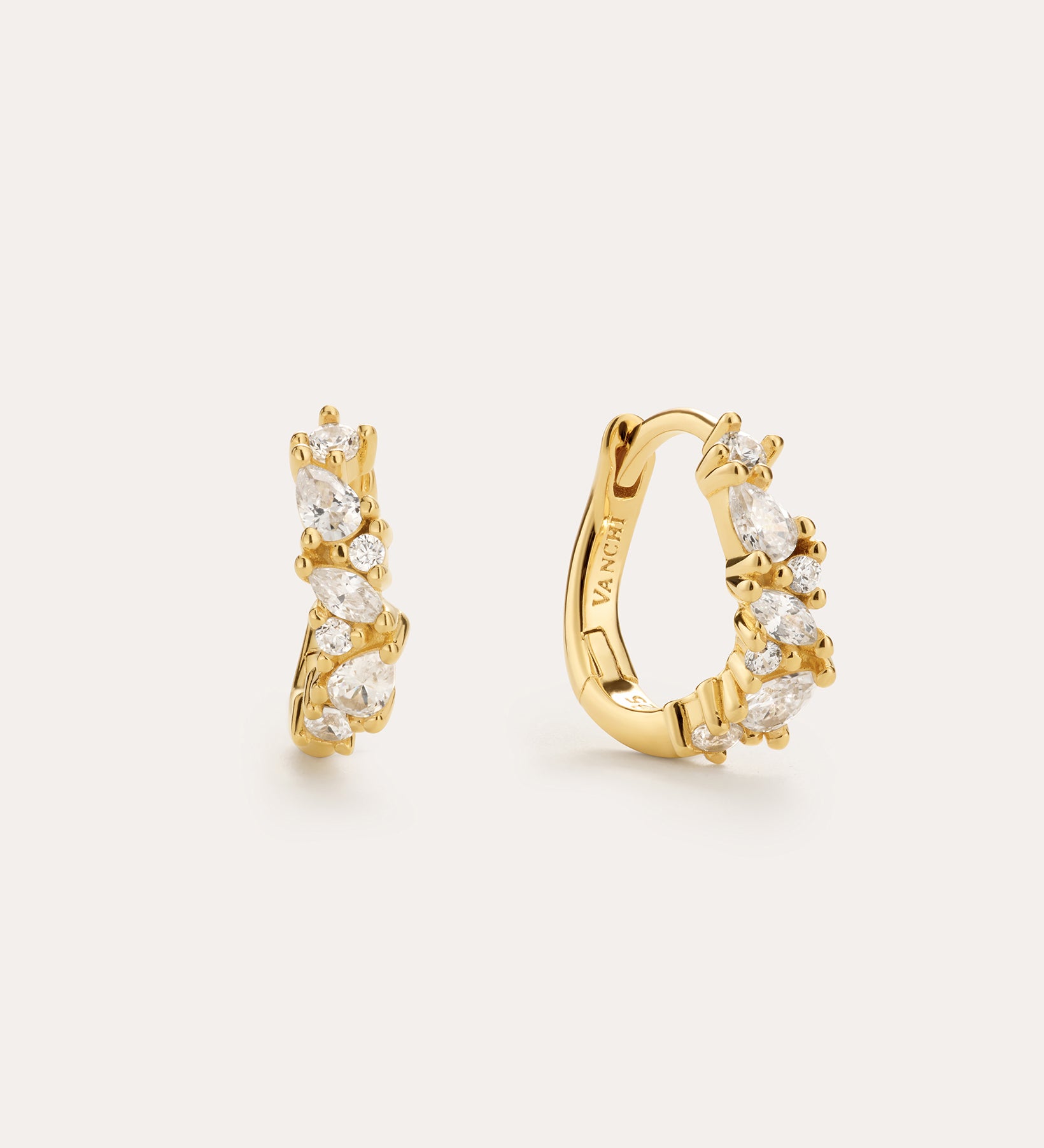 The Nori Twisted Crystal Huggies in Silver, plated in 18k gold, feature a clustered arrangement of marquise and round-cut cubic zirconia—perfect gold earrings to add sparkle to any look. Displayed against a light background.