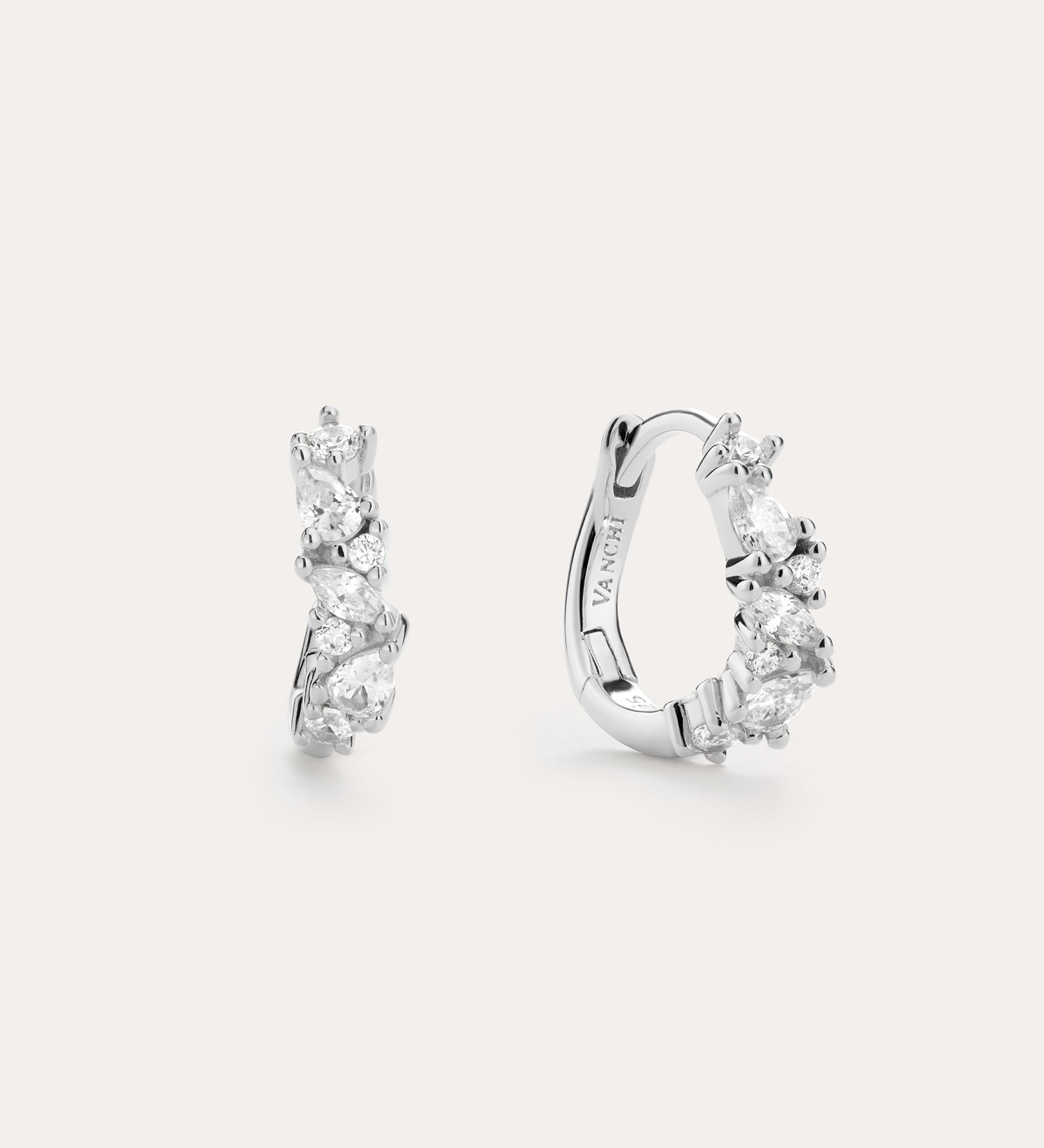 The Nori Twisted Crystal Huggies in Sterling Silver are chic hoops featuring multiple sparkling white crystals, beautifully showcased against a plain, light background.