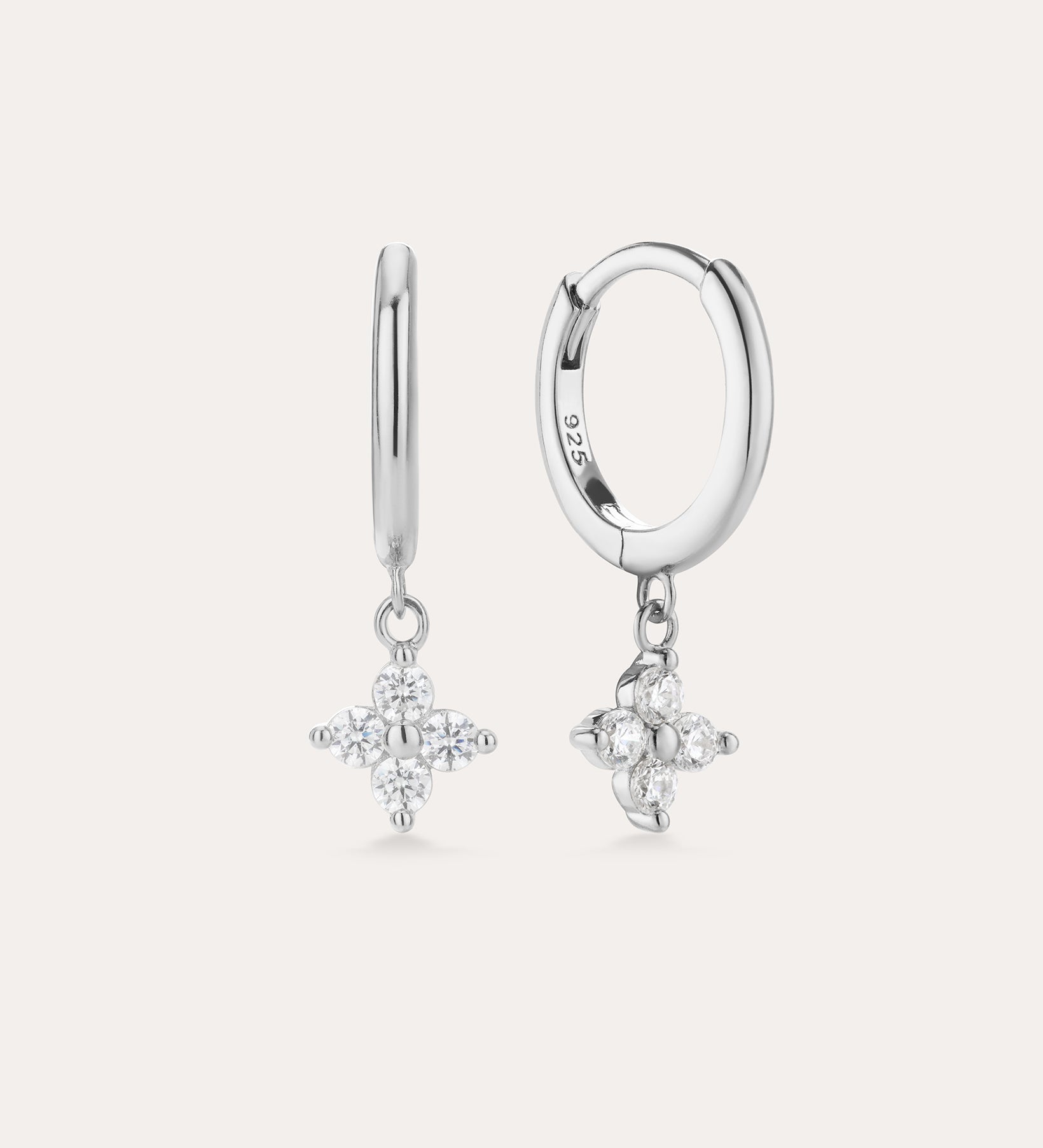 The Flora Crystal Charm Huggies in Sterling Silver feature dangling star-shaped charms with sparkling stones, shown against a plain light background.
