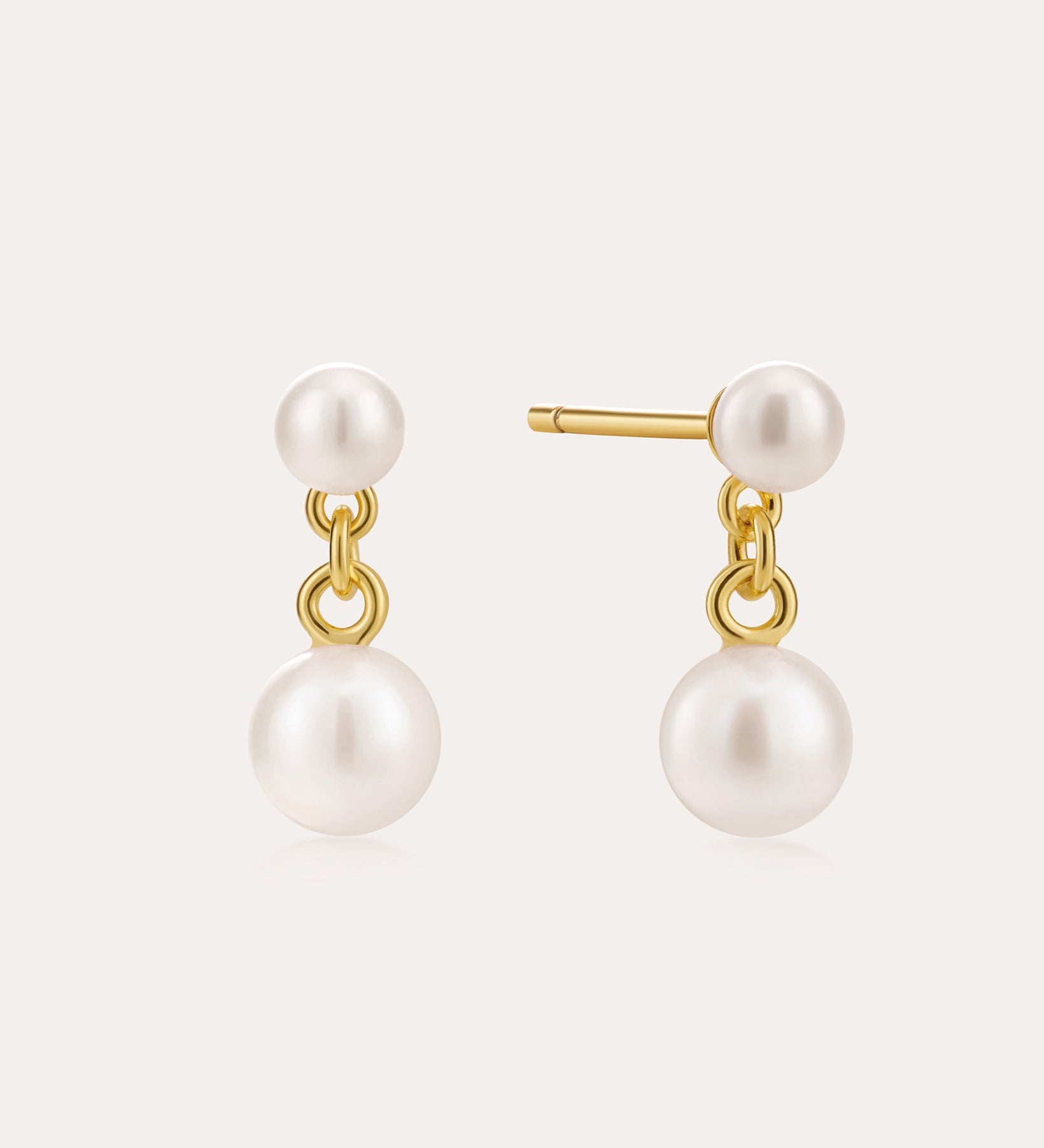 The Double Freshwater Pearl Drop Stud Earrings in Silver feature small and large round white freshwater pearls, with the larger pearls dangling below 18k Gold Plated studs against a light backdrop.