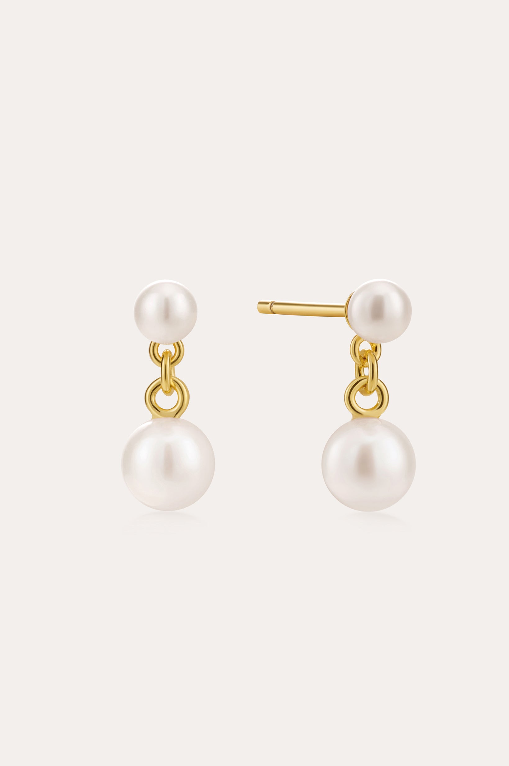 The Double Freshwater Pearl Drop Stud Earrings in Silver feature small and large round white freshwater pearls, with the larger pearls dangling below 18k Gold Plated studs against a light backdrop.