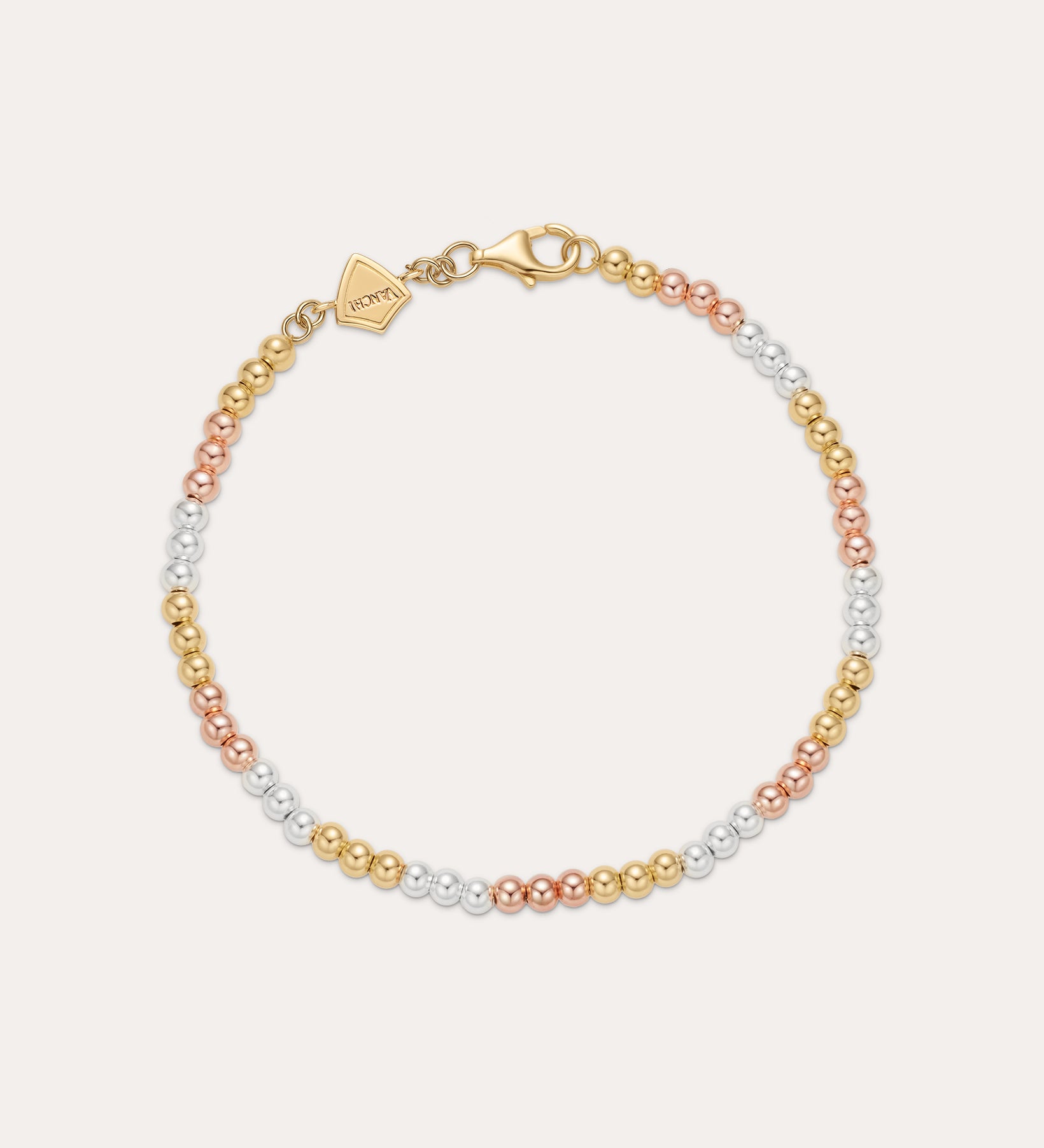 The Cecelia Three Tone Trinity Bracelet features small gold, sterling silver, and rose gold beads in a gradient pattern with a gold clasp and tag. This dainty bracelet is 18k gold plated and styled on a light background.