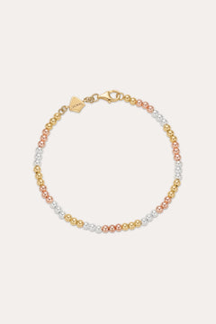 The Cecelia Three Tone Trinity Bracelet features small gold, sterling silver, and rose gold beads in a gradient pattern with a gold clasp and tag. This dainty bracelet is 18k gold plated and styled on a light background.