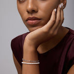 A woman with medium skin tone rests her chin on her hand, wearing a sleeveless burgundy top and the Celia Micro Freshwater Pearl Bracelet in Silver. She gazes thoughtfully at the camera with a neutral expression.
