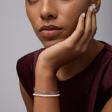 A woman with medium skin tone rests her chin on her hand, wearing a sleeveless burgundy top and the Celia Micro Freshwater Pearl Bracelet in Silver. She gazes thoughtfully at the camera with a neutral expression.