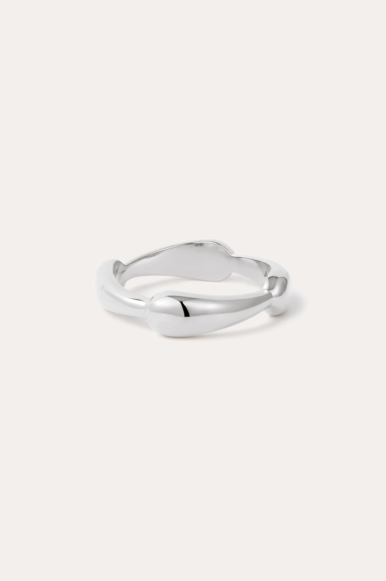 The Colette Link Droop Ring in Silver features a minimalist design with a smooth, slightly irregular band and rounded ends, shown against a light background.