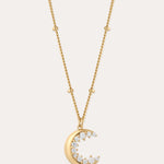 The Crescent Moon Crystal Charm Beaded Necklace in Gold features a beaded chain and a crescent moon pendant with sparkling clear stones, shown against a simple light background.