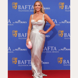 SPOTTED ON: Emily Norris wears Eden Trio Pearl Drop Earrings in Gold with a silver gown and pink clutch at the BAFTA Television Awards. She poses on the red carpet, with BAFTA and sponsor logos in the background.
