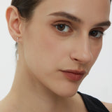 A close-up of a woman with fair skin and brown hair pulled back, wearing a black top and the Eden Trio Pearl Drop Earrings in Silver, looking slightly to the side with a neutral expression.
