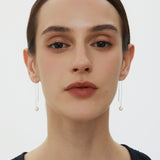 A woman with straight dark hair pulled back wears Eira Pearl Drop Threader Earrings in Silver and a sleeveless black top, facing forward against a plain white background.