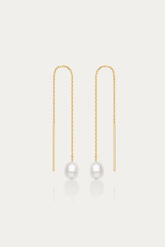 The Eira Pearl Drop Threader Earrings in Gold feature delicate chains ending with a single round white pearl, offering a minimalist and elegant look against a plain white background.